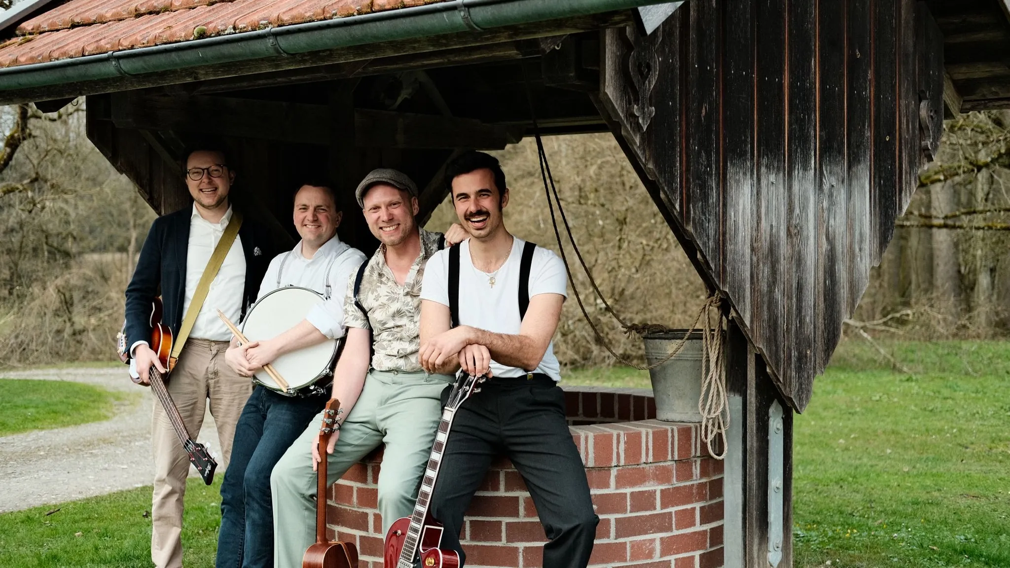 Hot Sausage am Brunnen unter einem Holzdach, vier Freunde mit Instrumenten